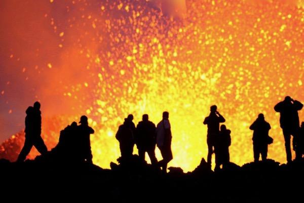 Silhouettes of people watching erupting volcano at night.
