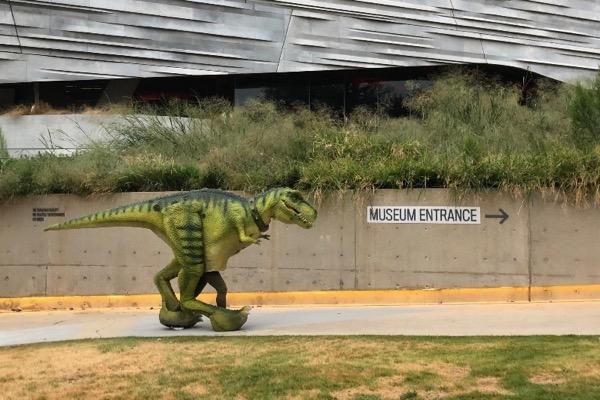 Green dinosaur sculpture near museum entrance sign.
