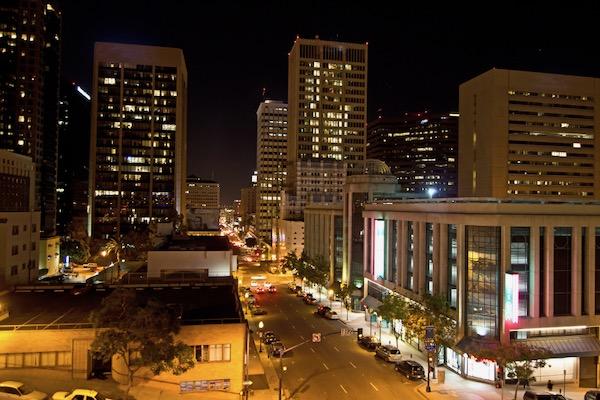 City street at night with tall buildings and lit windows.