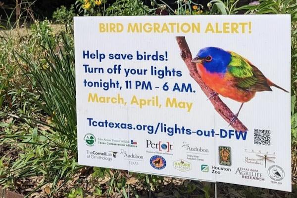 Sign with a colorful bird and text about bird migration alert and light reduction times.