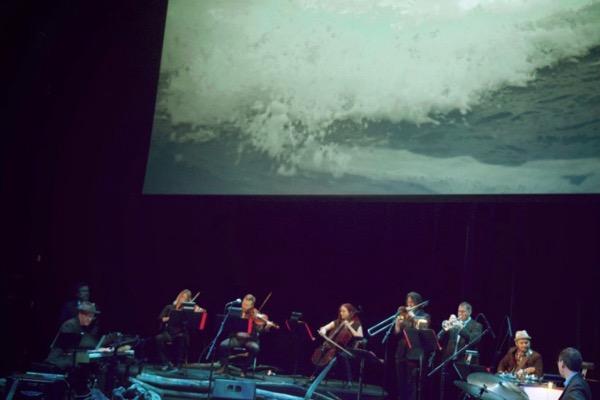 Orchestra performing under a wave projection.