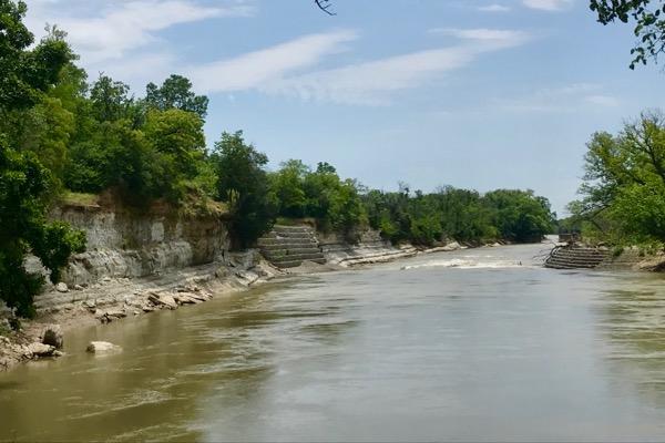 River with rocky banks and green trees under a clear blue sky.