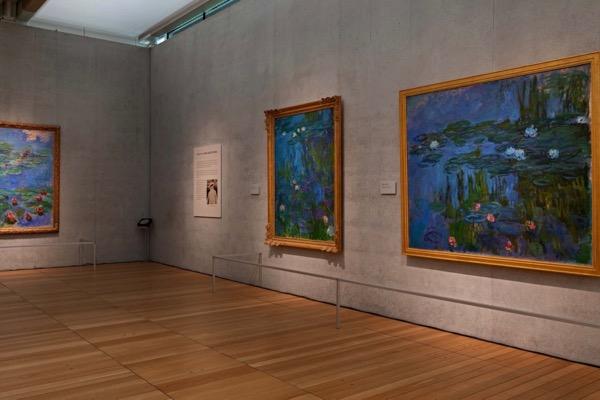Paintings in an art gallery with wooden floors and gray walls.