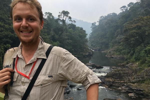Smiling person in front of a forested river.