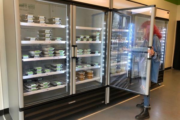 Person selecting meals from a large refrigerated display in a store.