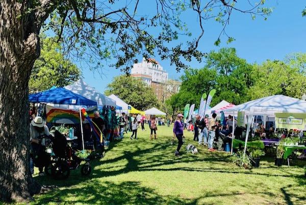 Outdoor market with tents, people, and trees under a clear blue sky.
