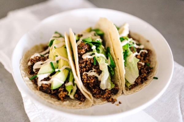 Three tacos with beef, avocado, lettuce, and drizzle on a white plate.