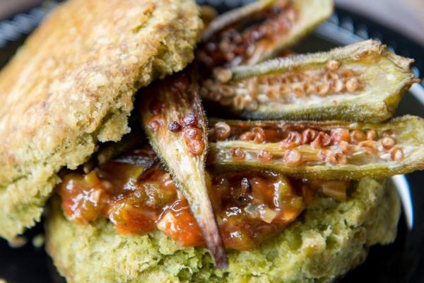 Split okra with biscuit and sauce on a black plate.