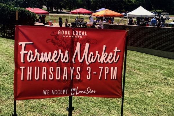 Red sign for a farmers market with tents in the background.