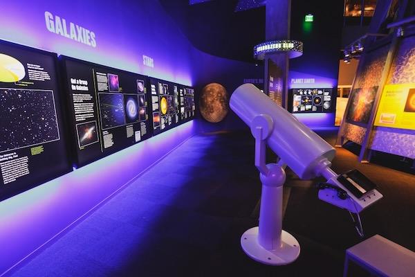 Interactive space exhibit with telescope, colorful displays, and celestial graphics.