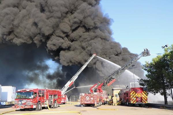 Firetrucks battling a large building fire with heavy black smoke.