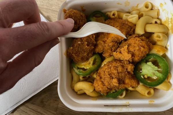 Fried chicken and jalapeños on mac and cheese in a to-go container.