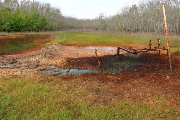 Abandoned rusty pipe structure in a grassy, marshy field.