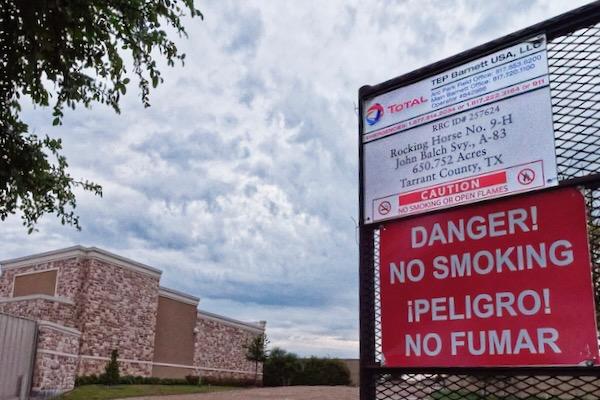 Red "No Smoking" sign on wire fence, cloudy sky background.