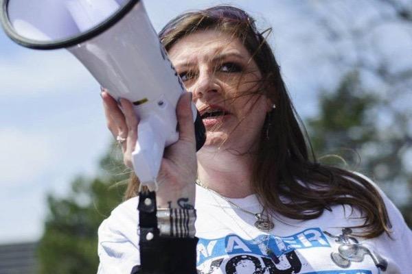 Woman speaks into a megaphone outdoors, wearing a white shirt.