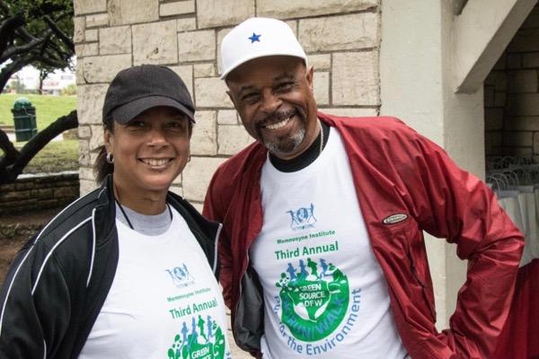 Two smiling people outdoors in matching event shirts and hats.