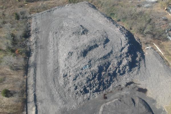 Large pile of gray gravel in a clearing, surrounded by trees.