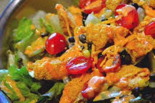 Colorful salad with lettuce, tomatoes, cheese, and orange dressing.