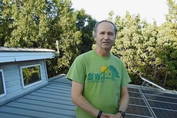 Man standing on a rooftop with solar panels and trees in the background.