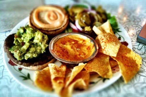 Platter with guacamole, chips, hummus, jalapeños, and pastries.