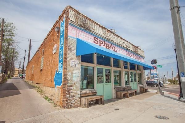 Brick corner building with blue awning and large windows under a clear sky.