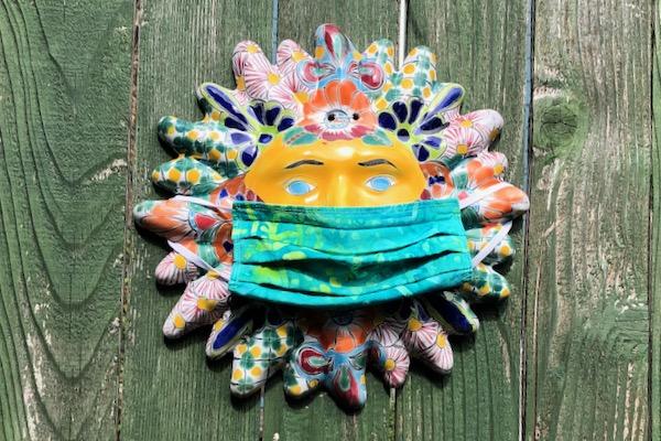 Colorful sun mask on wood wall, wearing a green face mask.