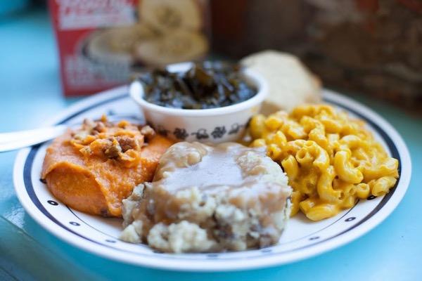 Plate with sweet potatoes, greens, biscuit, mac and cheese, and mashed potatoes with gravy.