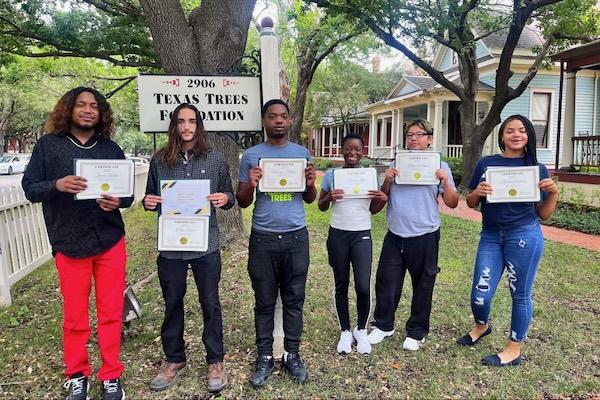 Six people standing outdoors, smiling, holding certificates.