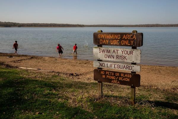 Lake with swimmers and a sign warning of no lifeguard.