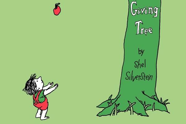 Child reaching for an apple near a large green tree.
