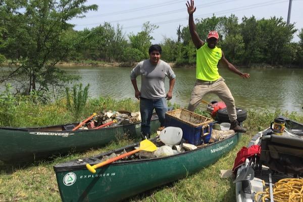 Two people pose with canoes full of supplies by a river.
