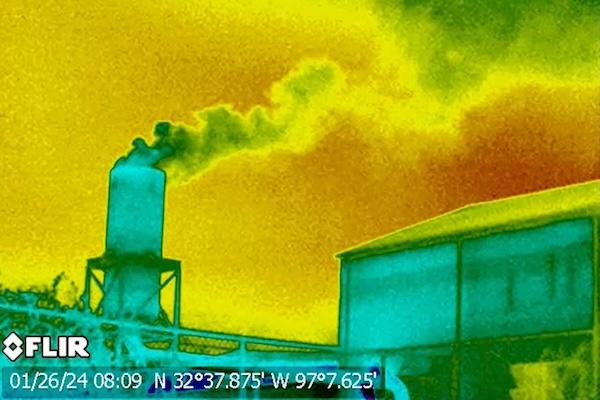 Thermal image of smoke billowing from a smokestack against a vivid yellow and orange sky.