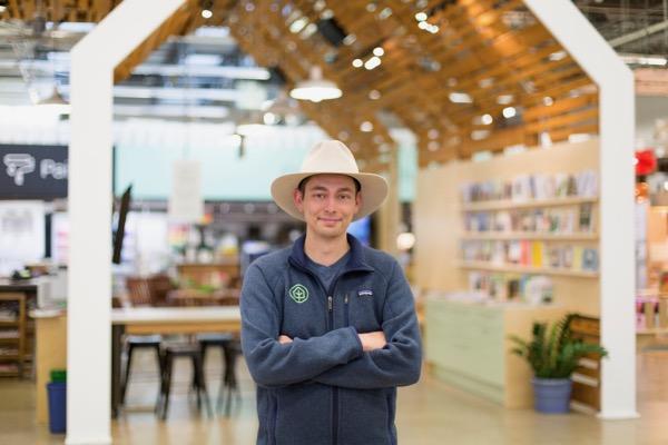 Man in a cowboy hat standing in a bookshop, arms crossed, smiling.