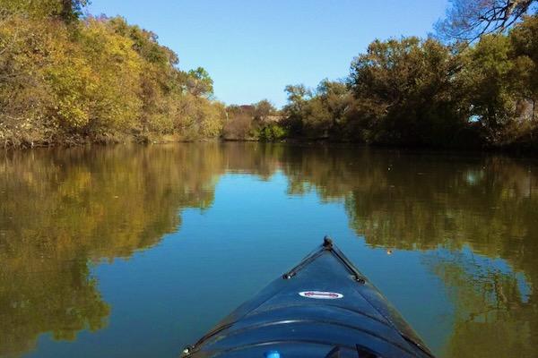 Kayak gliding on calm river, surrounded by autumn trees under a clear blue sky.