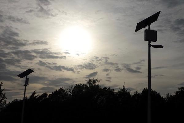 Solar panels against a cloudy sky with the sun shining through.