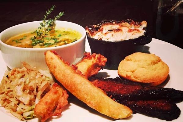 A plate with soup, cornbread, grilled meat, fried items, and cabbage.