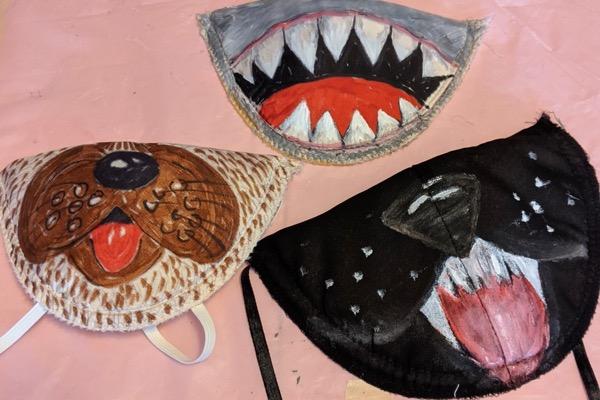 Three painted animal-themed masks: shark, dog, and cat designs on a pale background.