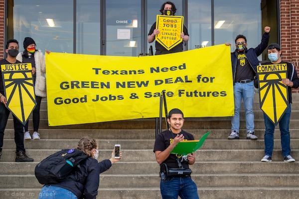 Protesters holding a yellow banner advocating for the Green New Deal on building steps.