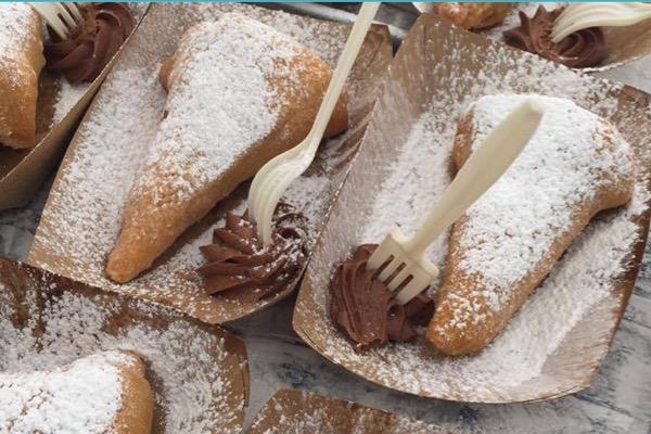 Pastries dusted with powdered sugar on paper trays with chocolate icing and forks.
