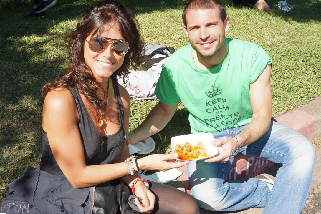 Two people sitting on grass, smiling, holding a plate of food.