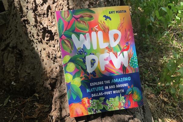 Colorful book titled "Wild DFW" leaning against a tree trunk.