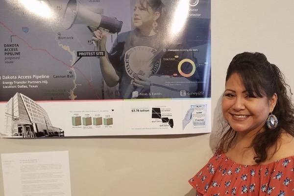 Smiling woman stands next to a collage with maps and diagrams on the wall.