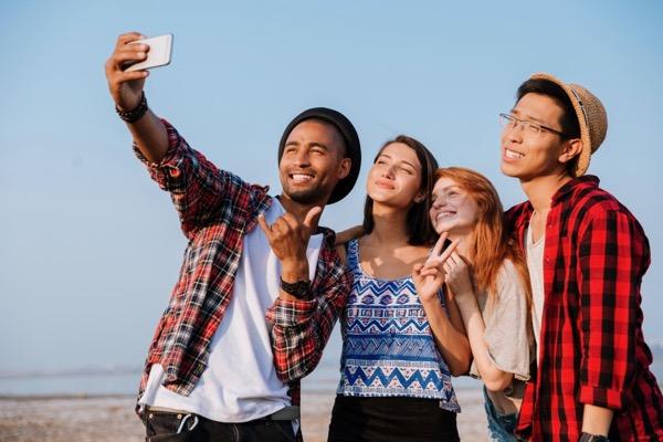 Group of friends taking a selfie outdoors, smiling under a clear blue sky.