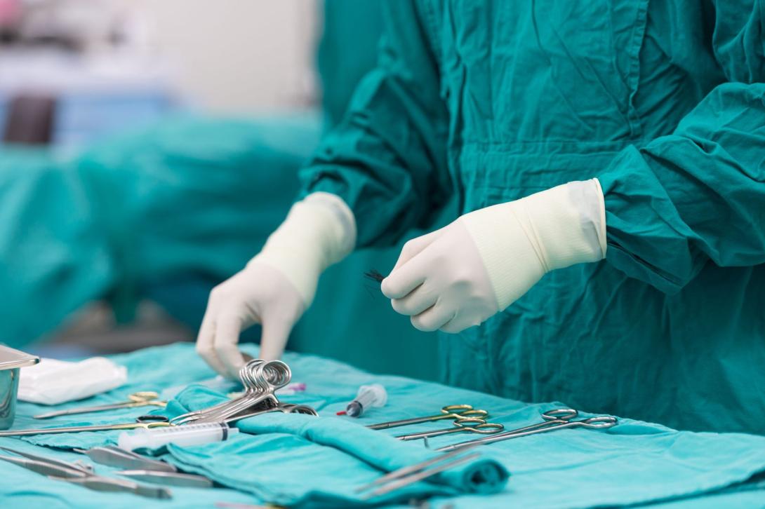 Surgeon in scrubs arranging surgical tools on a table.